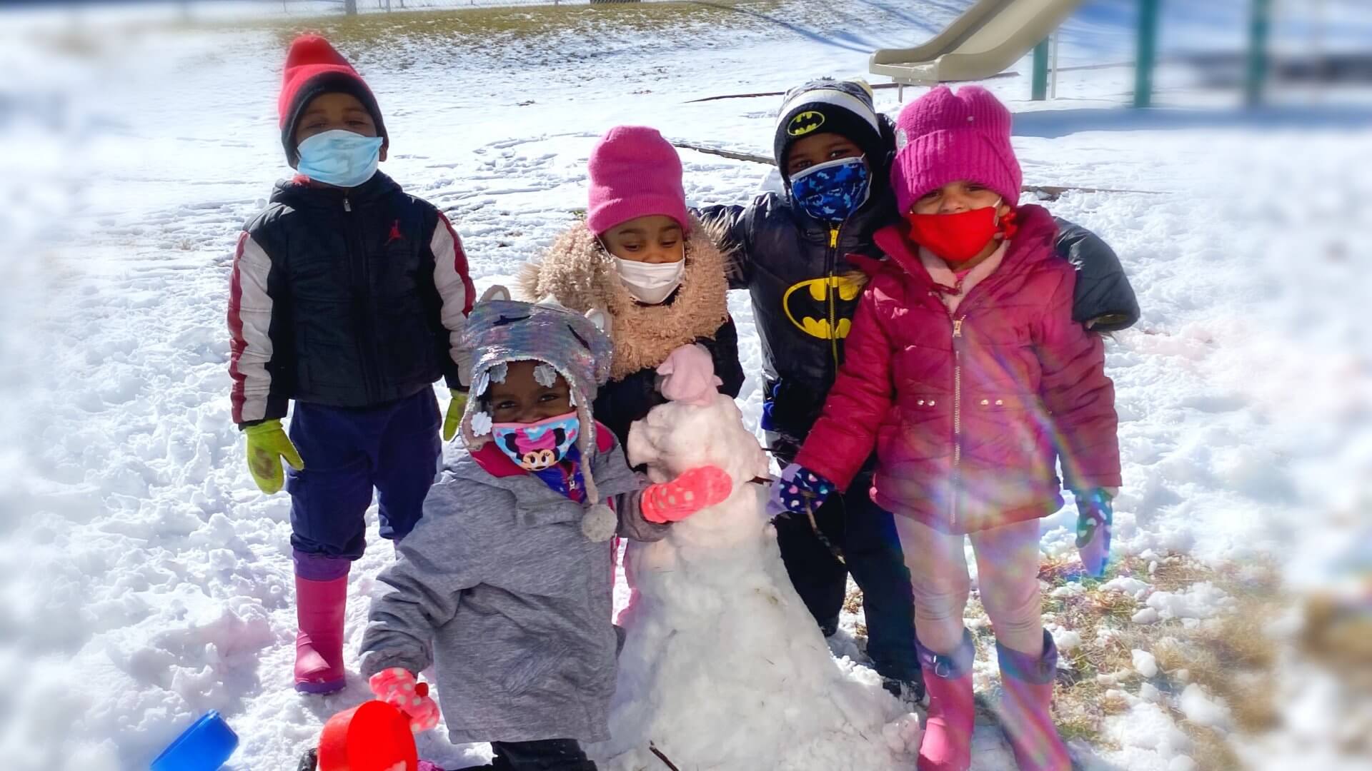 Four students play in the snow together as they start a snowman by the playground.