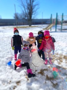 Four students play in the snow together as they start a snowman by the playground.